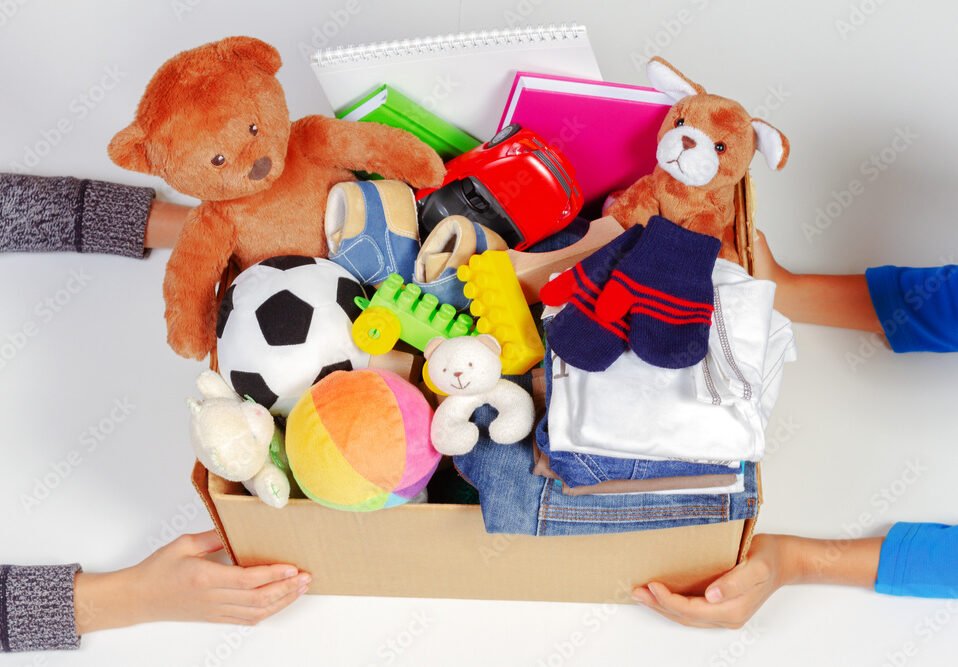 Donation concept. Kid hands with donate box with clothes, books, school supplies and toys, white background